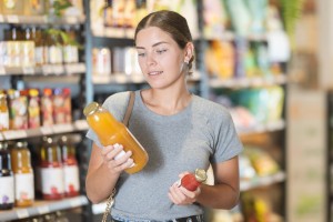 Etichetta Alimentare 300x200 Ragazza in un supermercato che legge l'etichetta di una bottiglia di succo di frutta