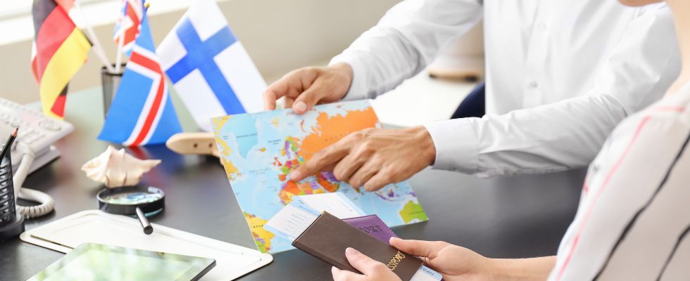 Tavolo di un ufficio con bandiere stati esteri e persona che indica un punto su carta geografica